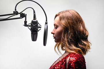 The singer sings in a recording studio, on the radio. In headphones, on a light background.