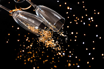 Two champagne glasses with golden sparkles over black background. Happy new year.