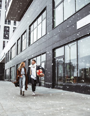 Happy young couple walking in the street with Christmas gifts presents in snowy weather. Christmas and holiday concept