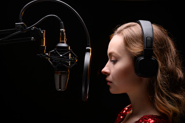 A singer or radio host is working in a recording studio with a microphone in headphones close-up,...