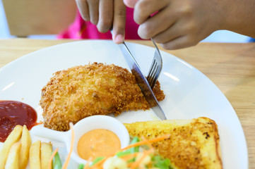 Close up knife and fork cutting grilled fish steak set in white dish on wooden table background.Salmon steak, french fries, bread and salad.Restaurant menu.