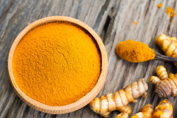 Turmeric powder in bowls and fresh turmeric on old wooden table. Herbal