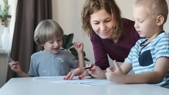 Two little boys sitting at the table at home and drawing together with their mom. Family concept