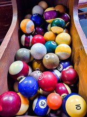 Fototapeta na wymiar Close up, selective focus on a wooden bin filled with colorful, old billiard table balls.