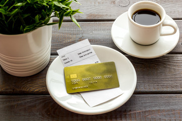 Paying in restaurant. Bank card near cup of coffee on dark wooden table
