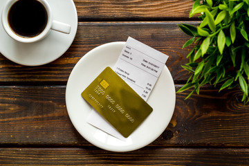 Paying in restaurant. Bank card near cup of coffee on dark wooden table top view