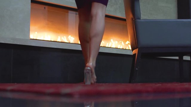Low angle slow motion video of female legs walking towards a fireplace. Beautiful model ankles in high heel's shoes.