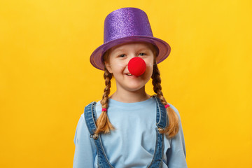 Funny child clown, hat and a red nose. Cheerful little girl on a yellow background. April 1. April...