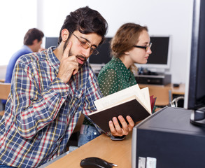 Focused man reading books in computer room of library