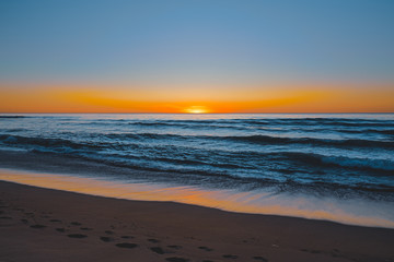 Abstract seascape. Beautiful tropical beach at sunset. Blue ocean, colorful sky, and sun setting down the horizon