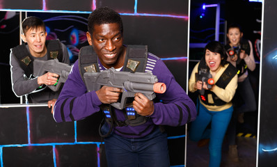 Fototapeta na wymiar Portrait of cheerful African-American with laser gun having fun on dark laser tag arena