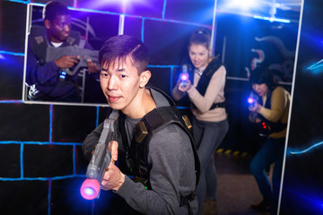 Emotional Asian man with laser pistol playing laser tag with fri
