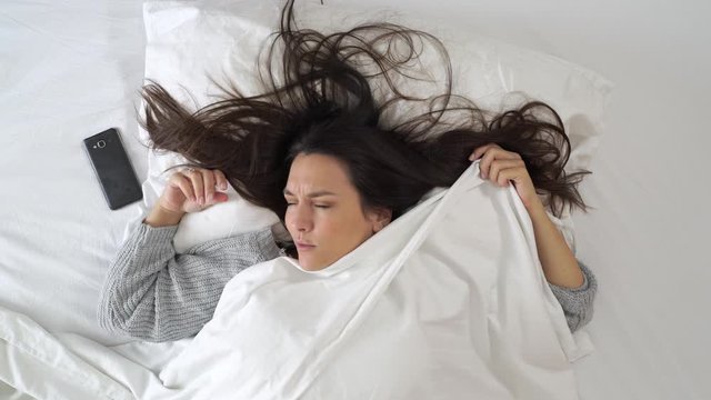 Woman waking up and hitting the snooze button on the cell phone.