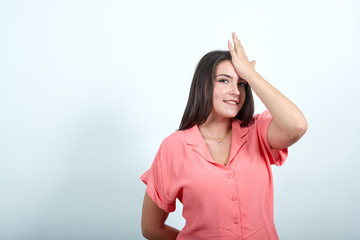 Attractive caucasian young woman in pink shirt keeping hand on head, smiling, holding other hand behind back isolated on white background in studio. People sincere emotions, lifestyle concept.