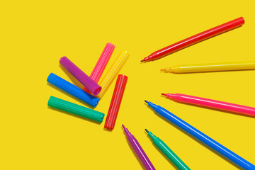set of new bright plastic opened colored felt pens lying on a yellow background near the caps . concept of office supplies