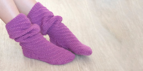 Female legs in high knitted socks of violet color on a beige background banner