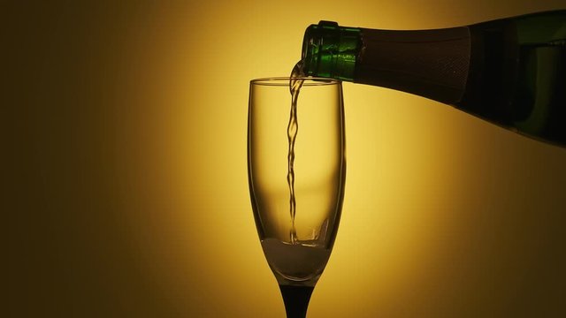 Champagne pouring in glass at yellow background. Party concept in slow motion. Nightlife. Close-up of glass of champagne
