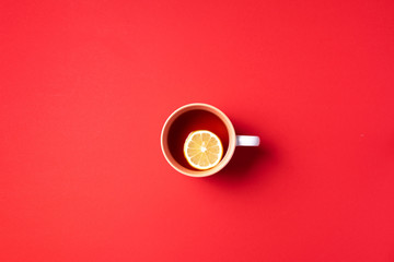 Cup of tea with lemon on red background. Top view. Copy space. Banner. Autumn or winter season concept