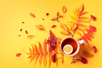 Autumn flat lay composition. Cup of tea, autumn bright leaves on yellow background. Top view. Flat lay. Autumn season concept