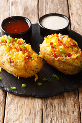 Stuffed potatoes with cheddar cheese, green onions and bacon served with sauces close-up on the table. vertical