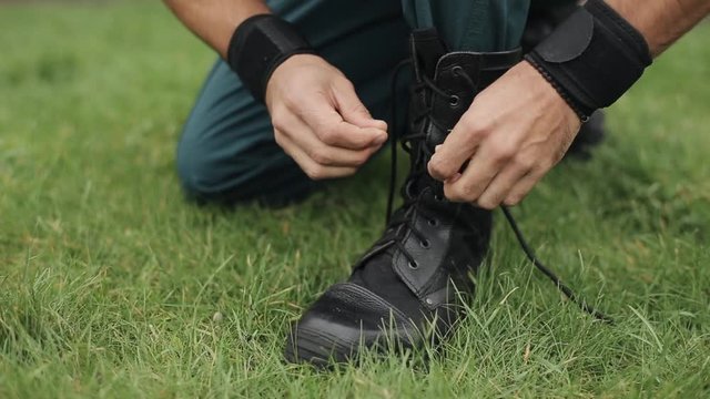 Close-up. Male hands tying shoelaces of his high black leather boots outdoors