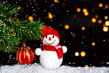 Snowman toy, Christmas balls, background with spruce branch, a group of elegant beautiful toys, on a black festive background with lights of lanterns and falling snow.