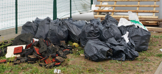 Construction site  debris in black plastic bags and broken wooden  boards to be thrown out onto a city lawn