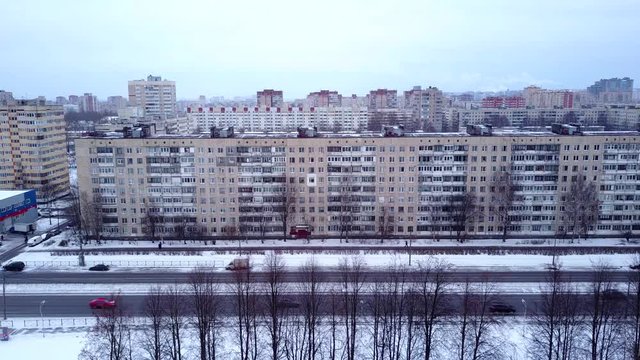 Front side of typical nine-storey residential house at dormitory area of Saint Petersburg city, aerial shot in winter time. Rather empty street along park seen downwards, Soviet Time panel and brick