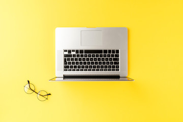 Business concept with laptop and eyeglasses on yellow background. Office desktop