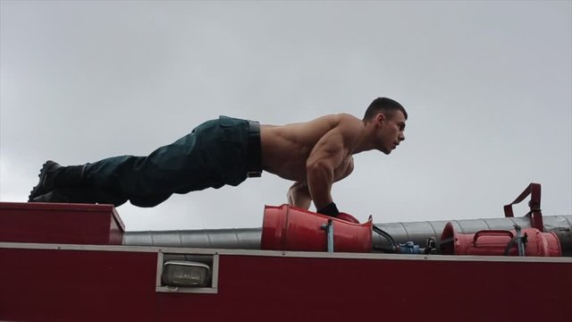 Strong man doing push-up on top of fire truck. Close view