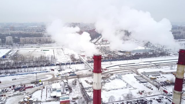 White smoke fly out from pair of chimney stacks, aerial shot in winter season. Industrial area seen downwards, city buildings at distance. Typical district heating plant at north area of city