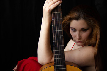 girl in a red dress sits on the floor near the guitar on a black background