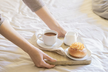 Hands holding wooden tray  with cup of coffee and sweet bun for Breakfast In Bed. Good morning relax concept.