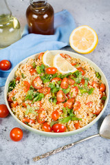 Tabouleh salad with tomatoes and fresh herbs in a plate is on the left in the frame on a concrete table with a copy of space. Traditionally an Oriental dish. Vertical orientation.