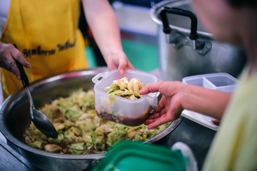 The hands of the needy holding a container to receive free charity food from volunteers : the concept of food assistance