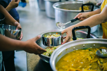 The hands of the needy holding a container to receive free charity food from volunteers : the concept of food assistance