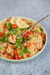 Tabouleh salad with tomatoes and fresh herbs in a plate with a spoon stands in the frame on a concrete table . Traditionally an Oriental dish.