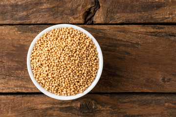 White mustard seeds in bowl on rustic wooden table. Top view