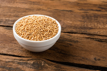 White mustard seeds in bowl on vintage wooden background. Close up