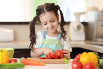 happy child girl chopping tomatoes on cutting board with knife in kitchen