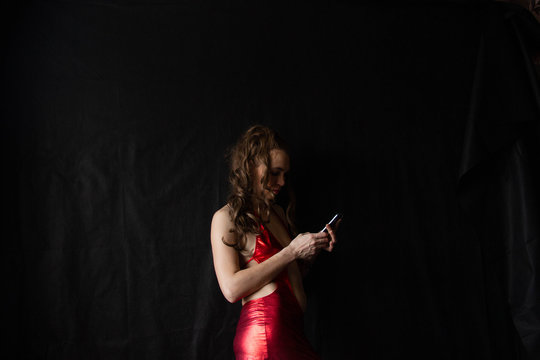 portrait of a sexy girl with long hair in a short dress with an open back on a black background. in the hands of the phone