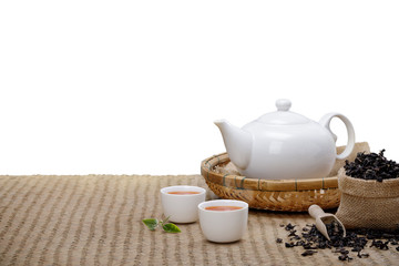 Warm cup of tea with teapot, green tea leaves and dried herbs on the bamboo mat at morning isolate...