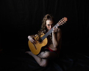 girl in a red dress sits on the floor near the guitar on a black background