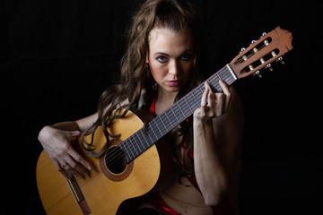 girl in a red dress sits on the floor near the guitar on a black background