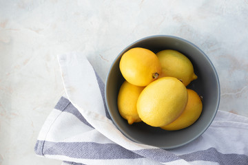 Raw fresh yellow lemon in bowl and towel on marble table, top view. Organic ripe citrus fruits with copy space