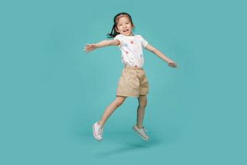 Playful energetic Asian little girl jumping in mid-air, empty space in studio shot isolated on colorful blue background