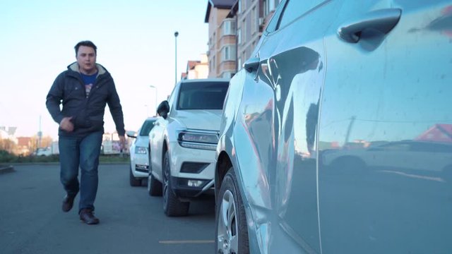 Guy going to parking lot and seeing his car is crashed. Man is very upset due to accident with door, he crying, screaming, hysterically beating his fist or head at door, spitting on it and leaving