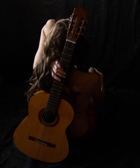 Fototapeta na wymiar girl in a red dress sits on the floor near the guitar on a black background
