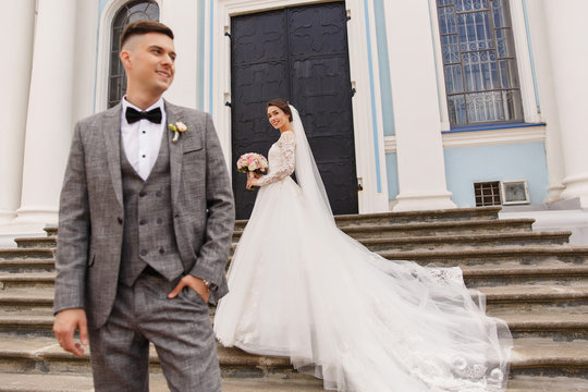 Wedding photography of stylish newlyweds. Beautiful wedding couple, elegant groom in grey suit and happy bride in white wedding dress with long train posing at wedding day