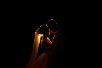 Fotobehang Creative idea of wedding photography at night. Silhouette of a bride and groom illuminated by a lights © Wedding photography